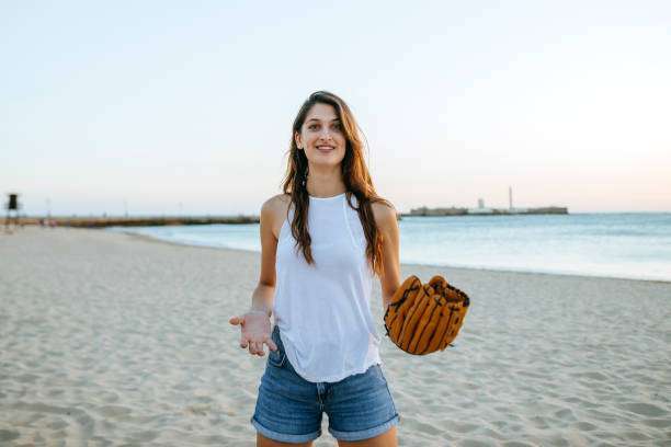 A young woman is holding a baseball glove on the beach