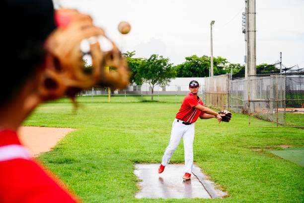 A playful man teaching a boy baseball exercises outdoors on a sunny day at a public park. baseball glove