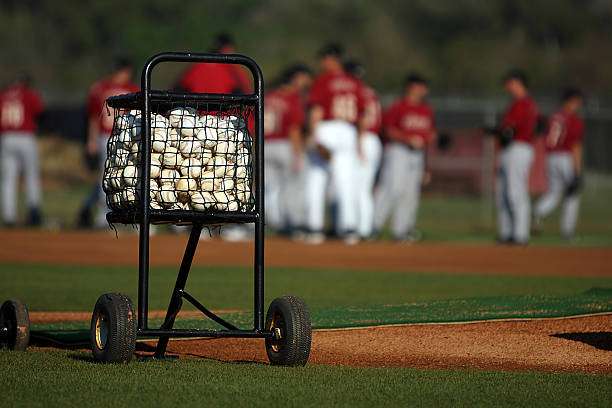 A large cart overflowing with baseballs sits on the field, perfect for baseball glove drills.