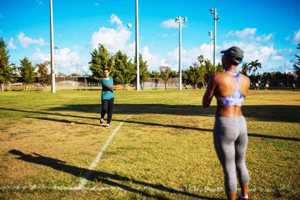 Adults playing catch on a sunny baseball field; one will need a baseball glove.