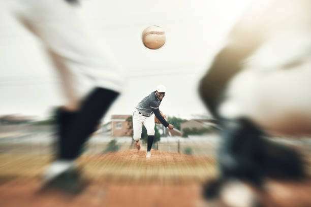 Blurry action shot of a pitcher throwing, other players with baseball gloves nearby.