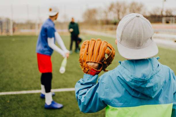 Child in blue jacket holds a baseball glove, preparing to play catch on a field.