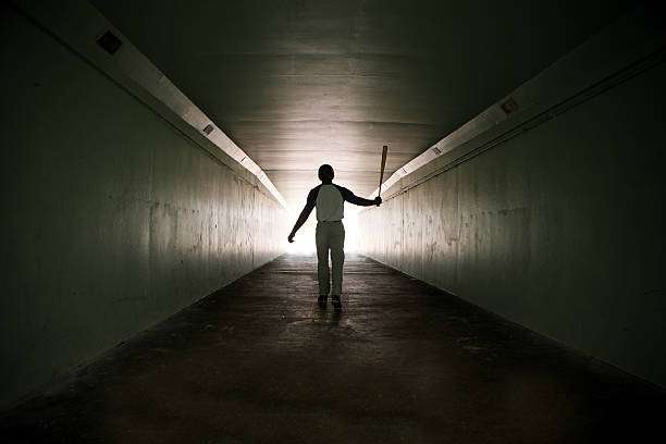 Silhouette of a person with a baseball bat walking through a tunnel, needing a baseball glove.
