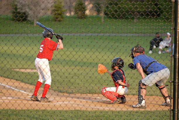 Young player at bat, with a catcher wearing a baseball glove and an adult coach.