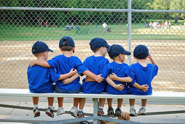 Five young baseball players in blue uniforms sitting on a bench with a baseball glove.