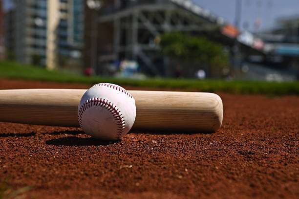 A baseball and wooden bat await play on a dirt field, needing a baseball glove.