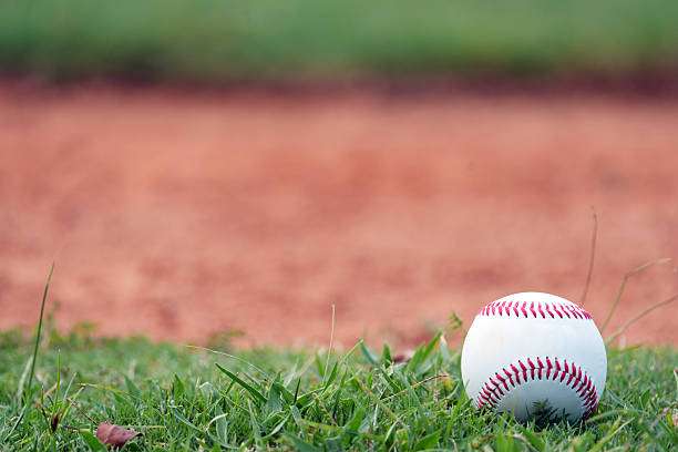 A baseball lies in the grass, ready for a player and their baseball glove.