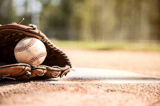 A worn baseball and leather baseball glove rest on the dusty infield.