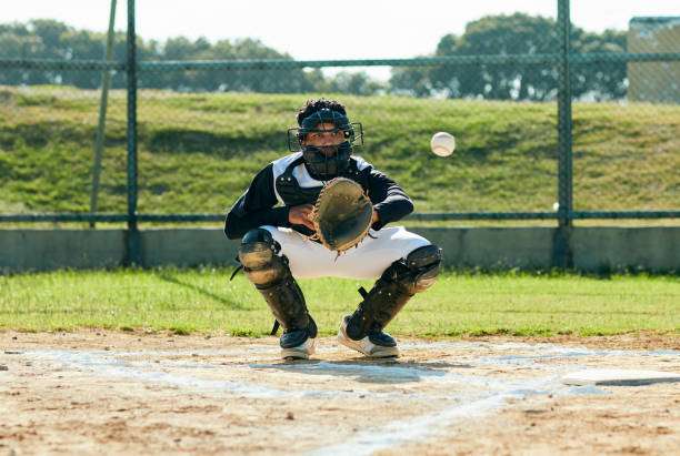 Baseball catcher in full gear squats, focused on catching a pitch with his baseball glove.