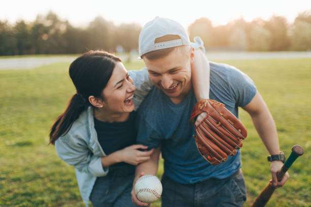 Laughing couple on a field, man holding a baseball with his baseball glove.