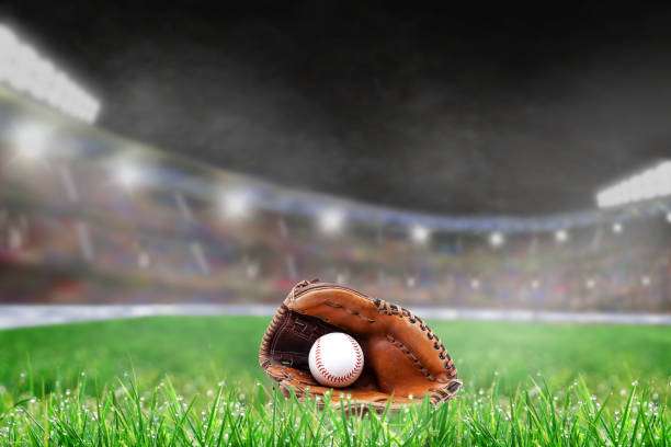 Baseball glove and ball on grass in brightly lit outdoor stadium.